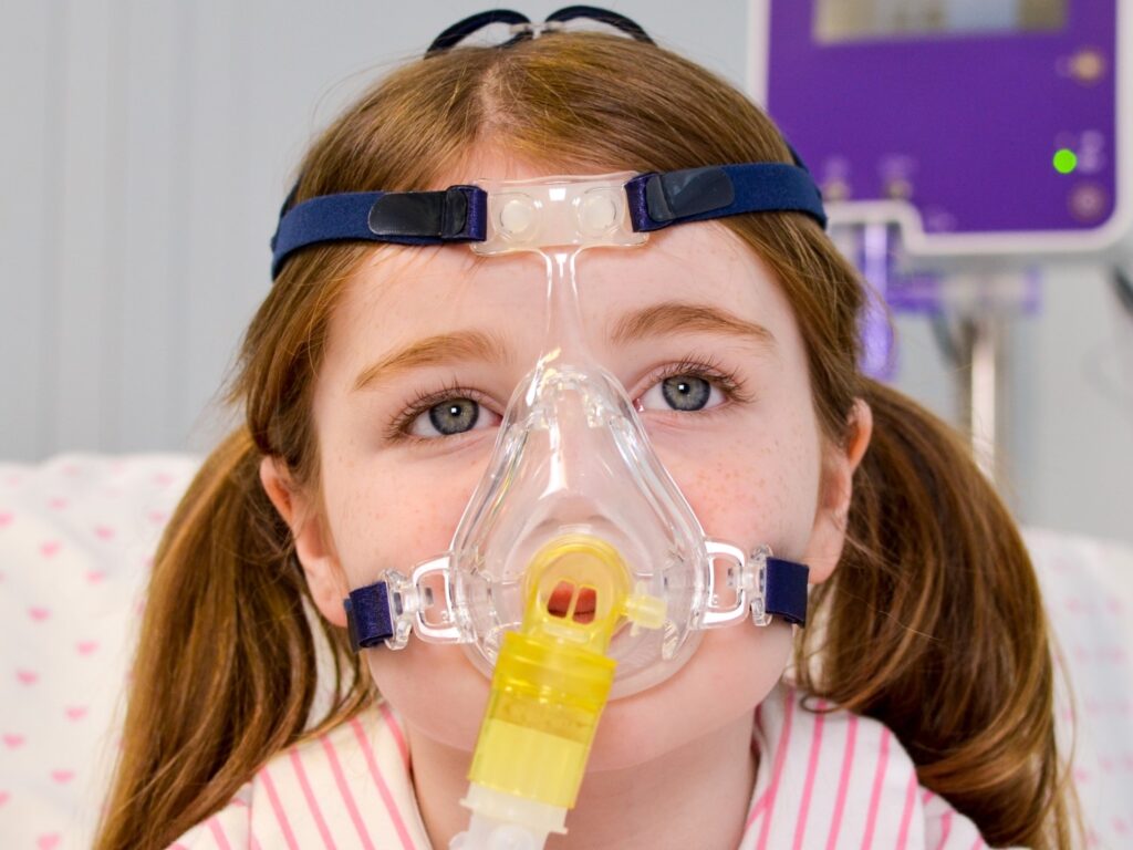 A young girl wearing an NIV non invasive ventilation full face maskconnected to an Armstrong Medical FD140i device for CPAP