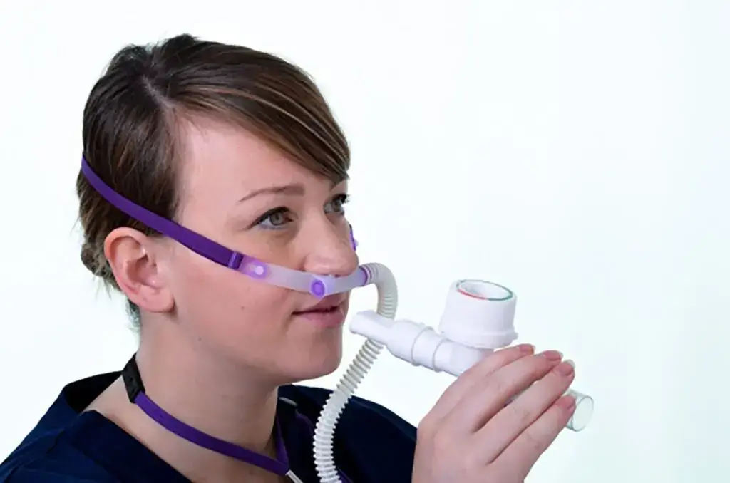 A woman wearing an Armstrong Medical AquaNASE nasal cannula, holding an Ultra-PEP.
